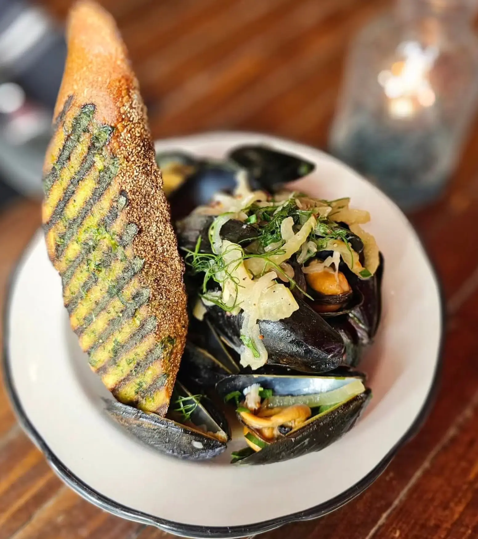 Steamed mussels with herbs and grilled bread in a white bowl.