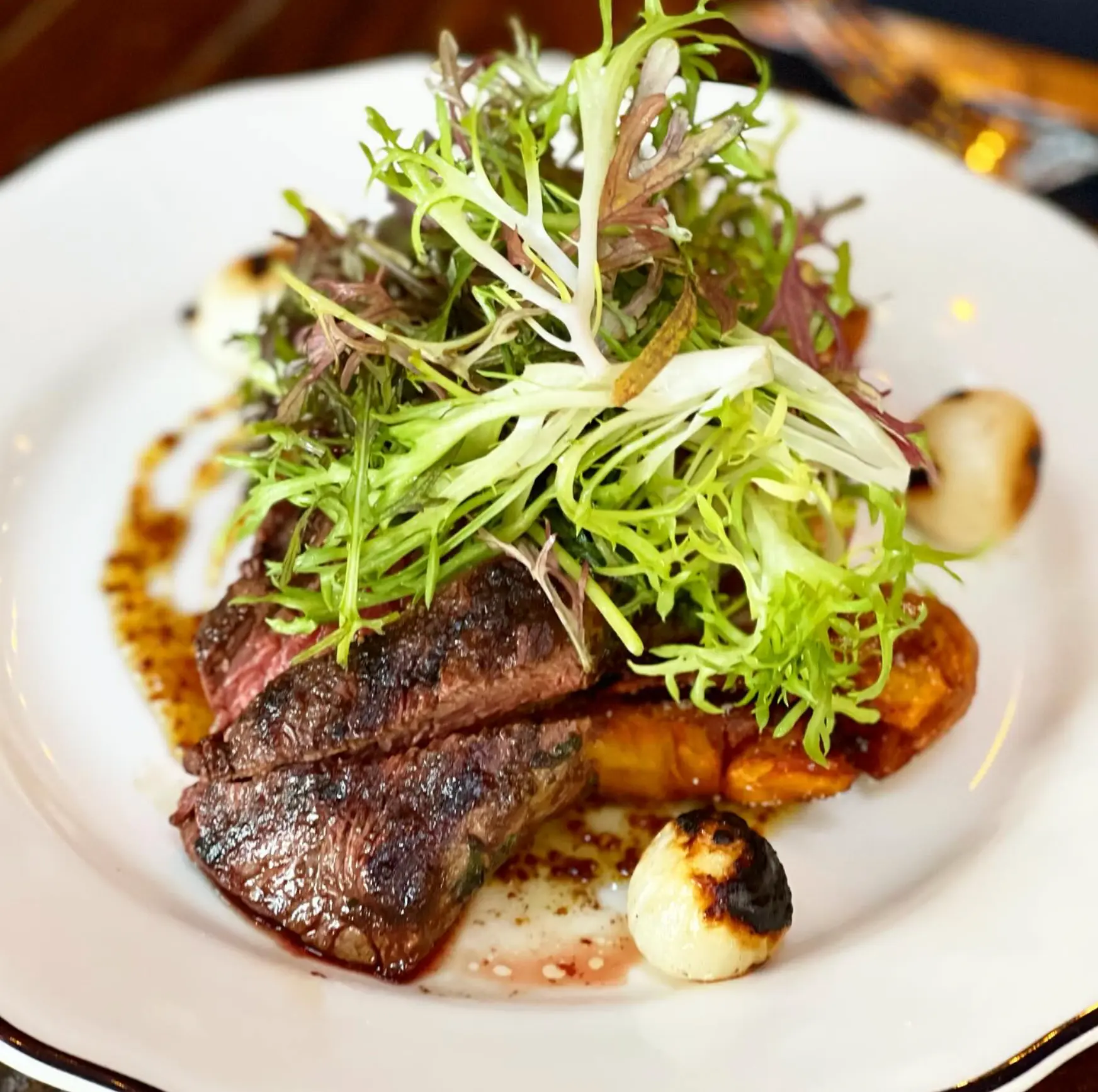 Sliced steak with potatoes, salad and charred onions.
