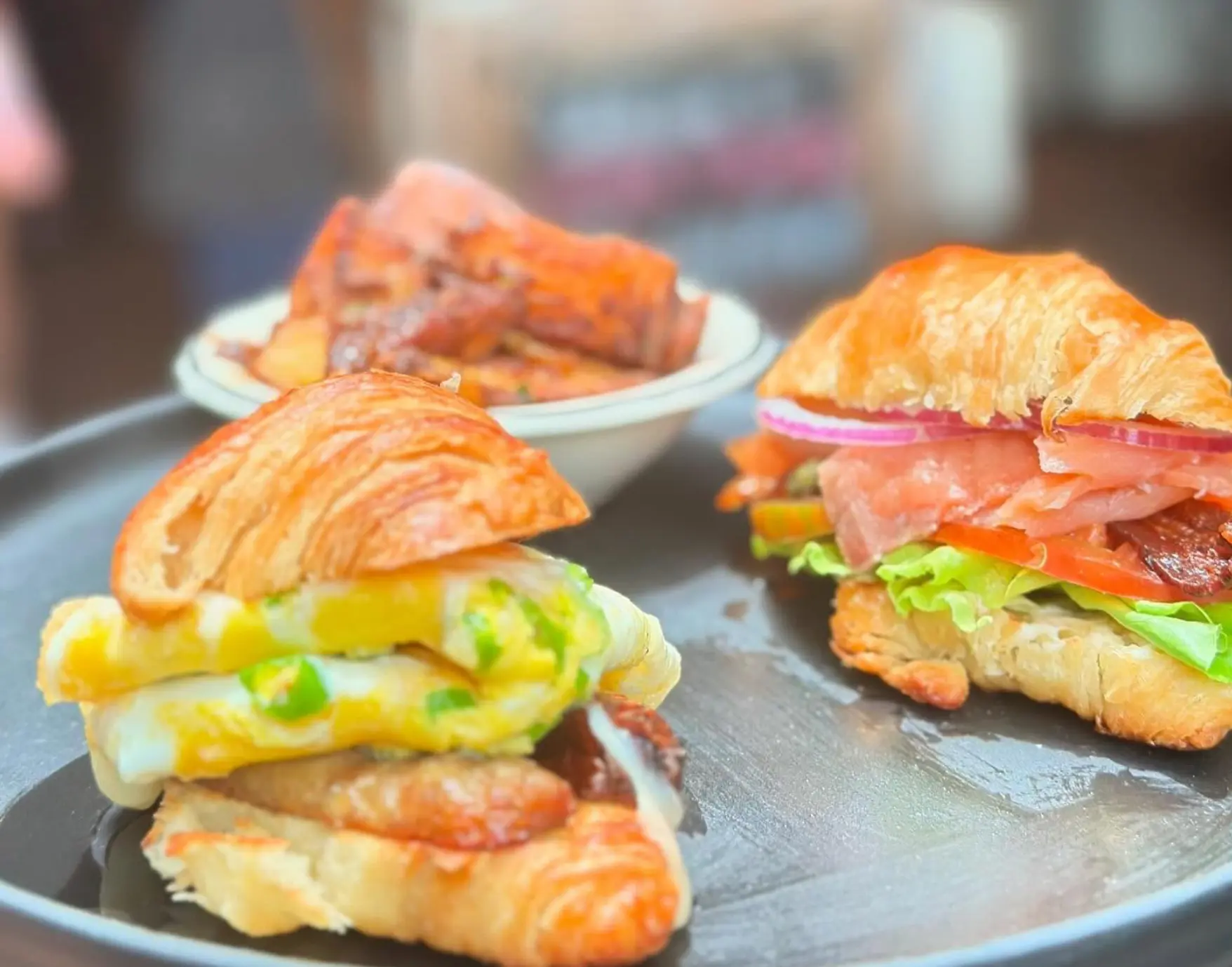 Two croissant breakfast sandwiches with breakfast potatoes.