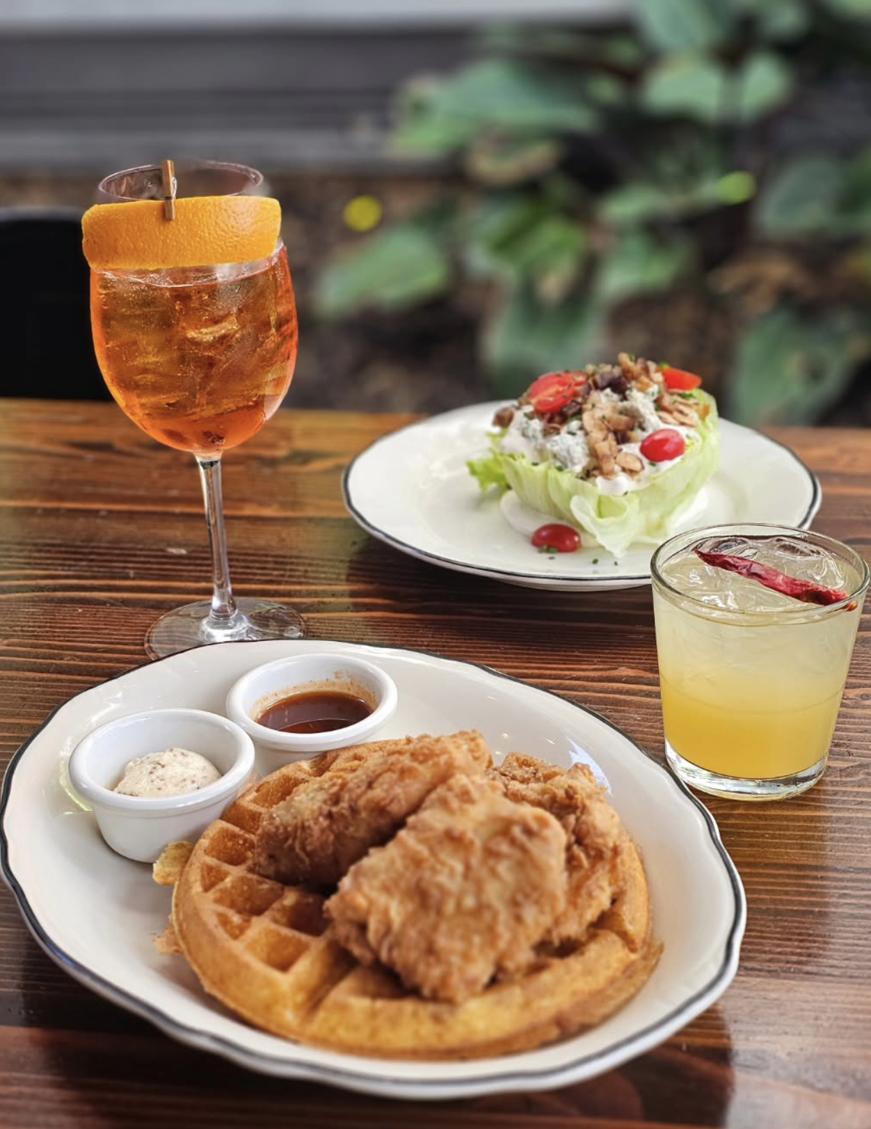 Fried chicken over a golden waffle on a patio table, with a spritz and an iced cocktail.