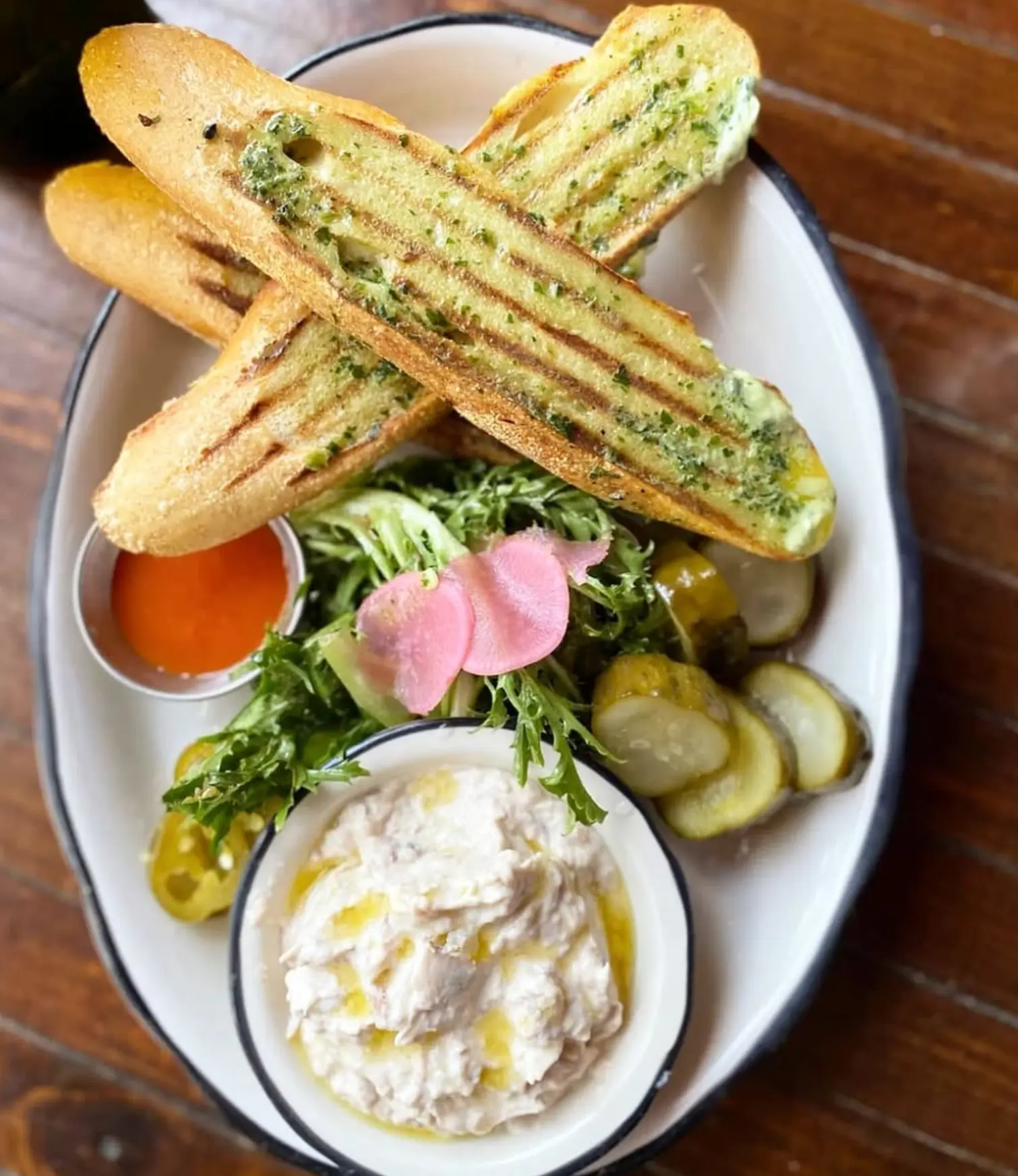 Grilled bread with creamy dip, greens, pickles and peppers.